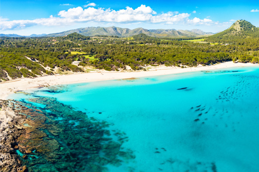 Cala Agulla op Mallorca met helderblauw water en parelwit strand, met groene bergen op de achtergrond